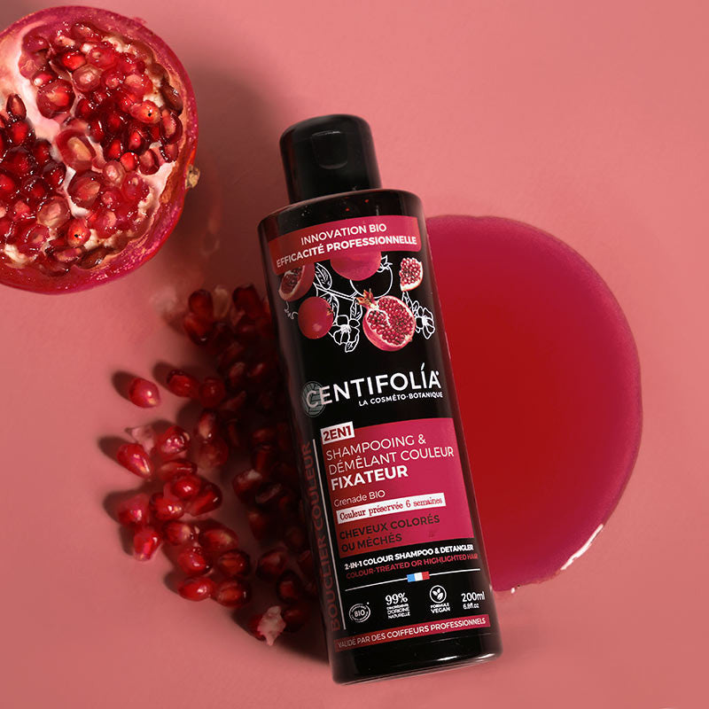 Centifolia 2 in 1 Colour Shampoo and Detangler (Wholesale) from above laying in a puddle of the red coloured shampoo, Half a pomegranate and pomegranate seeds are beside it