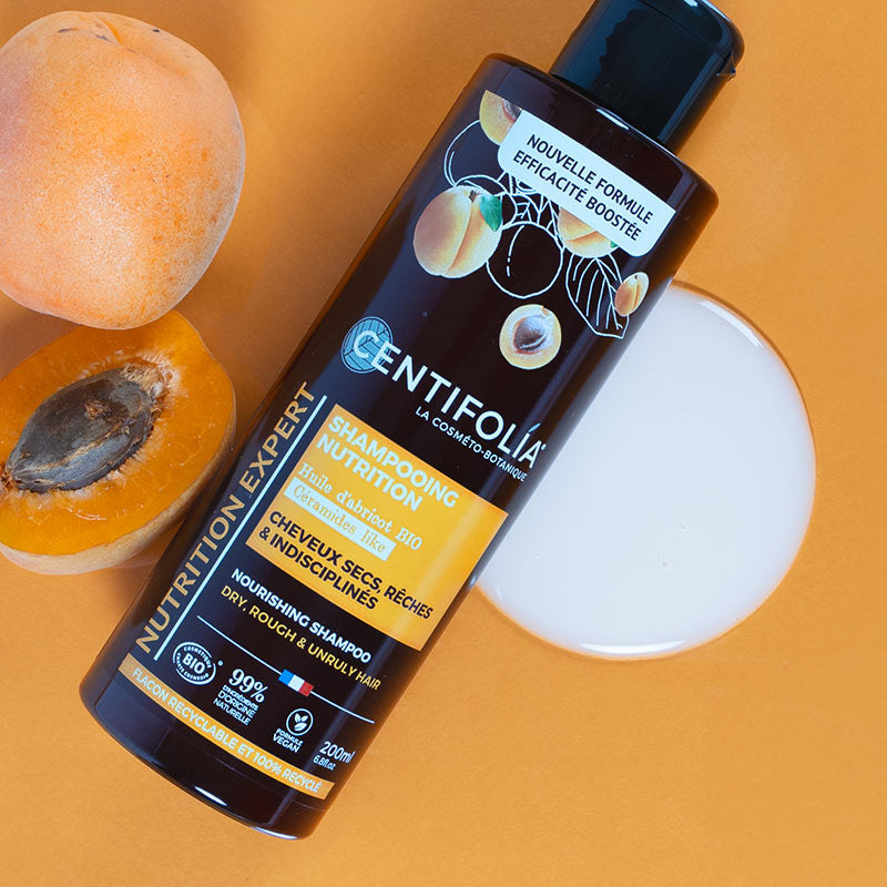 Centifolia organic Nourishing Shampoo for Dry, Rough & Unruly Hair (Wholesale) from above in a puddle of the shampoo. Apricots are beside the bottle signifying them being a key ingredient